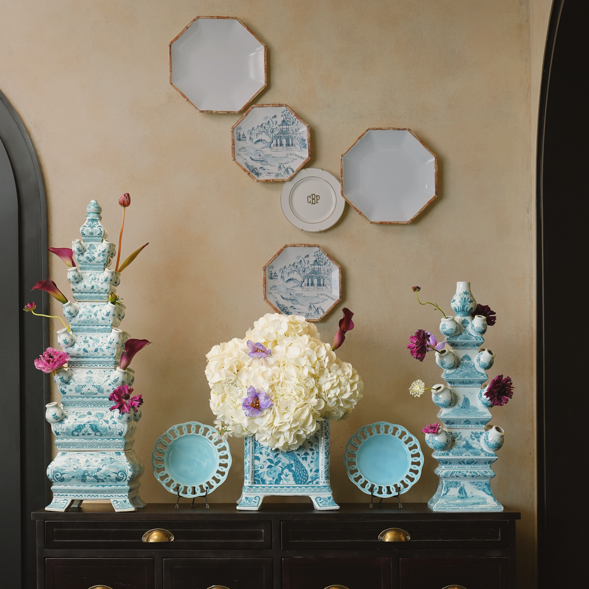 Decorative setup with blue and white ceramic pieces on a dark wooden dresser against a beige wall.