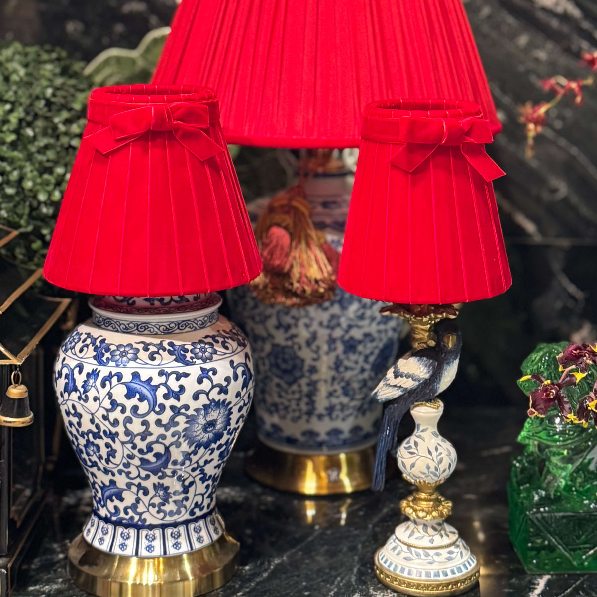 Three red pleated fabric lampshades with matching red bow details, displayed on decorative blue-and-white porcelain table lamps against a dark marble wall.