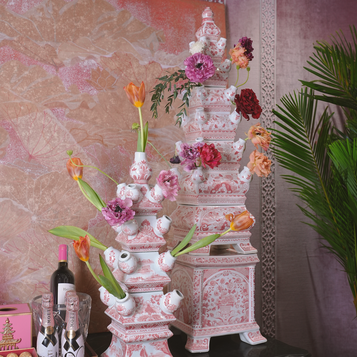 Decorative pink ceramic tower with floral arrangements against a patterned wall.