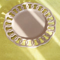 A close-up of a decorative ceramic plate with an intricate scalloped cutout rim, set on a yellow tablecloth alongside other matching tableware.