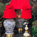 Three red pleated fabric lampshades with matching red bow details, displayed on decorative blue-and-white porcelain table lamps against a dark marble wall.