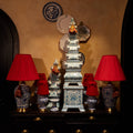 A decorative display featuring a tall blue-and-white porcelain pagoda-style tower centerpiece, flanked by two matching blue-and-white ceramic lamps with bright red fabric shades, set on a dark wooden cabinet against a warm beige wall.