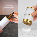 A cylindrical white and gold portable battery pack shown in a split demonstration: on the left, a hand inserts a battery into the detachable unit with text reading 'Detachable'; on the right, a hand holds the unit above a separate white charging pad with text reading 'Undetachable battery'.