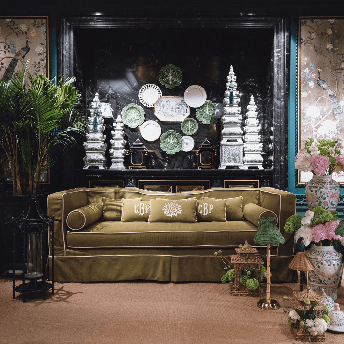Stylish living room featuring an olive green sofa with monogrammed pillows and an elegant backdrop of decorative plates.